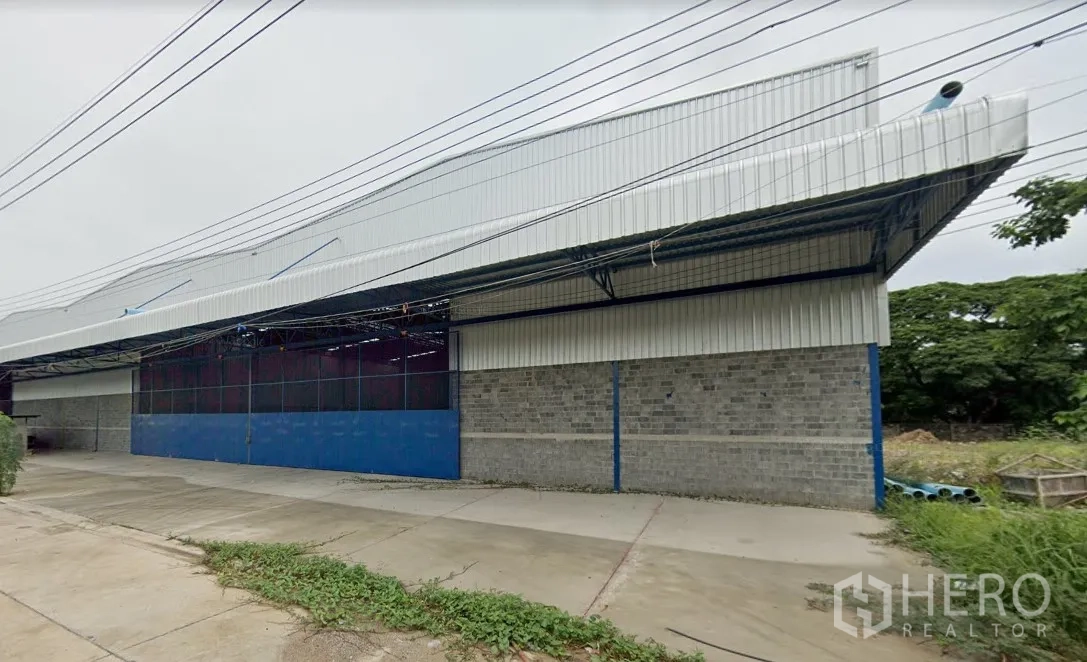 Warehouse for rent in Min Buri, Bangkok - Steel-clad warehouse exterior in Min Buri, Bangkok with high gabled roof, blue sliding gate, and wide concrete loading apron.
