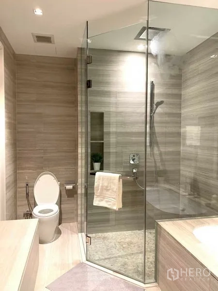 Condominium for rent in Watthana, Bangkok - Contemporary bathroom with glass shower, toilet and light wood-look tiles.