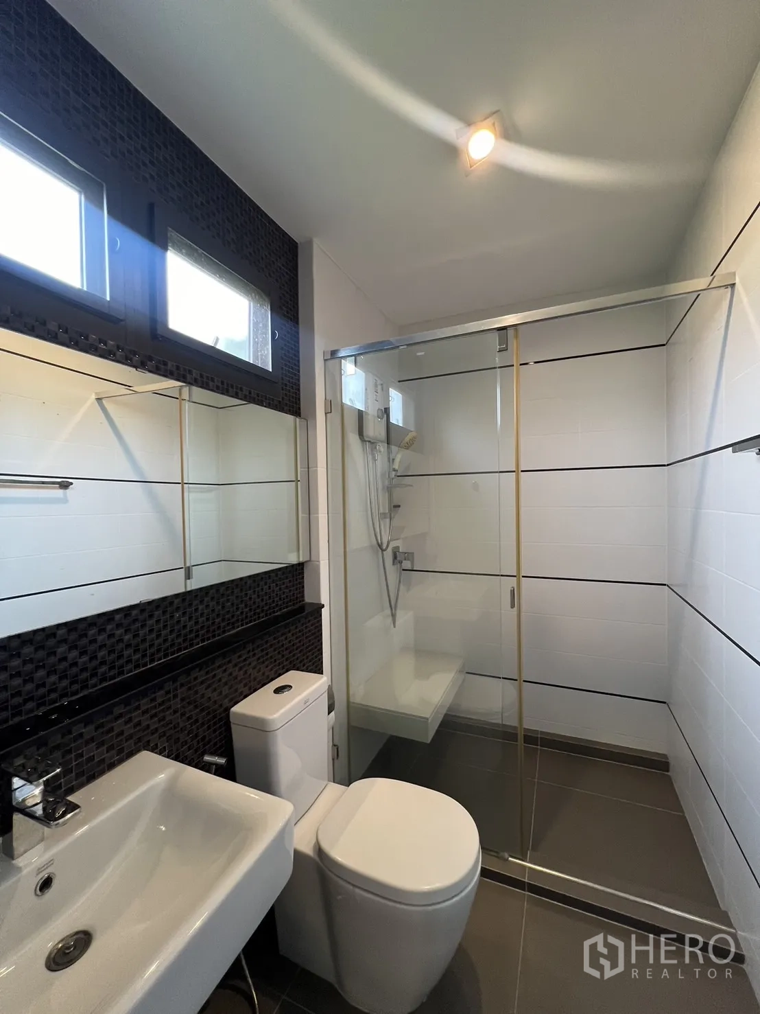 联排别墅 出租在Lat Phrao, Bangkok - 衛浴配無框玻璃淋浴間、白色檯面盆與深色裝飾牆。