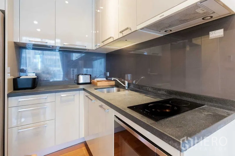 Condominium for rent - Sleek L-shaped kitchen with glossy cabinets, cooktop, and sink.
