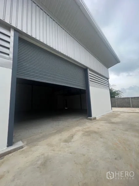 Warehouse for rent or sale in Sai Noi, Nonthaburi - Large roller shutter door partially open on warehouse with spacious apron.