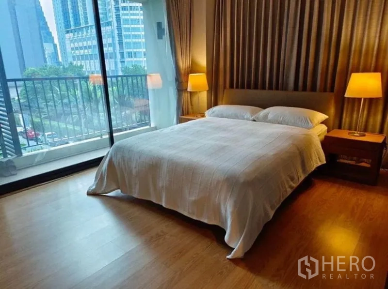 Condominium for rent in Watthana, Bangkok - Master bedroom with floor‑to‑ceiling glass and balcony overlooking greenery.