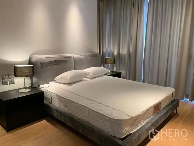 คอนโด ให้เช่าในKhlong Toei, Bangkok - ห้องนอนใหญ่เตียงบุนวมสีเทา โต๊ะข้างสองฝั่ง และผ้าม่านทึบ