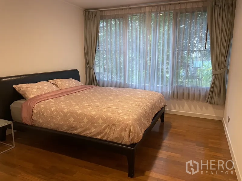 Condominium for rent in Pathum Wan, Bangkok - Spacious master bedroom with king bed and wide corner windows framed by drapes and tree views.