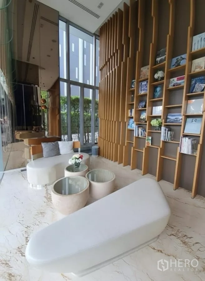 Condominium for rent in Watthana, Bangkok - Reading lounge with floor‑to‑ceiling bookshelves and modern seating by a glass wall.