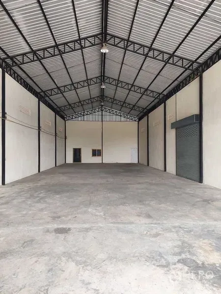 货栈 出租在Pathum Thani - 仓库长进深无柱空间，金属屋顶与混凝土地面，侧墙设卷闸门。