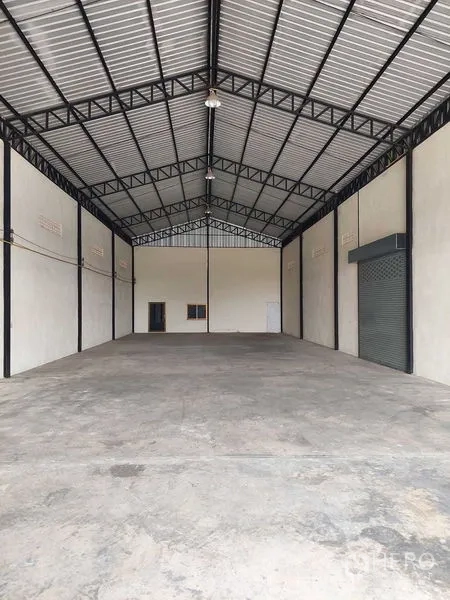 货栈 出租在Pathum Thani - 仓库长进深无柱空间，金属屋顶与混凝土地面，侧墙设卷闸门。