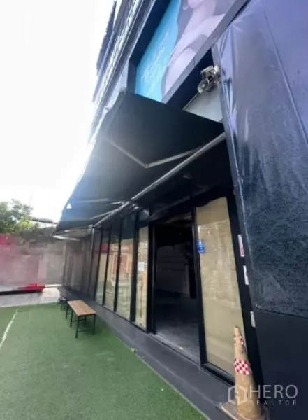 พื้นที่ขายปลีก ให้เช่า - มุมมองด้านข้างของหน้าร้าน แสดงกันสาดยื่นออก กระจกประตูเข้า และม้านั่งด้านหน้า