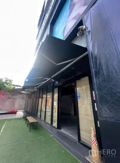 พื้นที่ขายปลีก ให้เช่า - มุมมองด้านข้างของหน้าร้าน แสดงกันสาดยื่นออก กระจกประตูเข้า และม้านั่งด้านหน้า