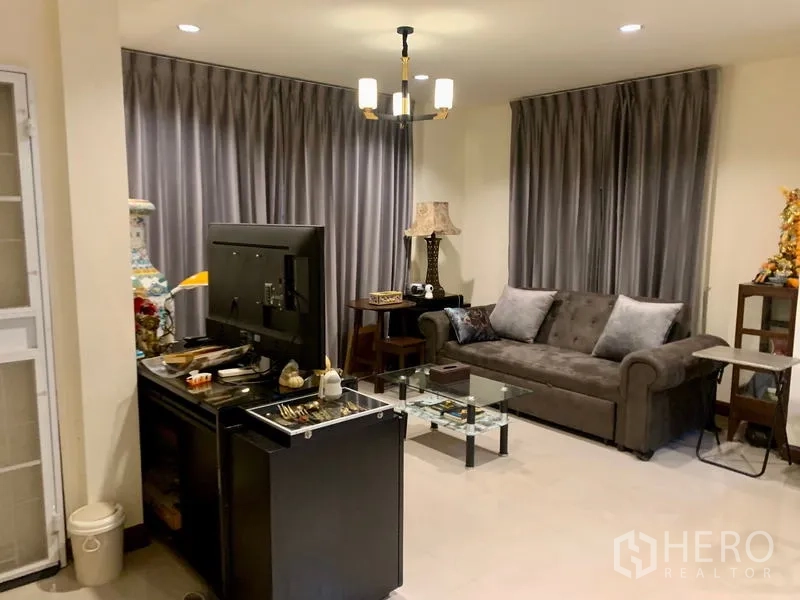 Detached House for rent in Khlong Sam Wa, Bangkok - Lounge setup with sofa, TV stand, glass table, and modern chandelier.