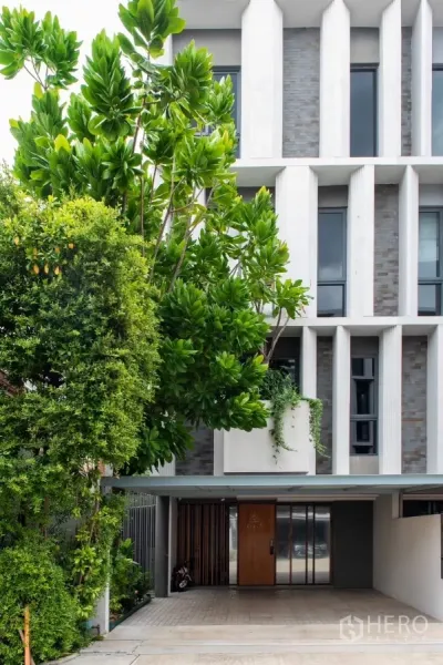联排别墅 出租在Lat Phrao, Bangkok - 现代联排别墅立面，带有遮蔽车位和繁茂绿植。