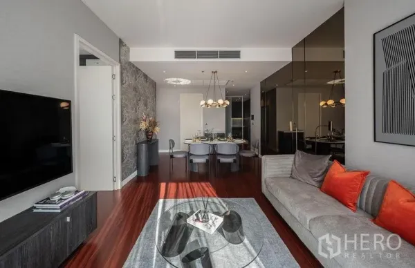 公寓 出租在Watthana, Bangkok - 曼谷瓦他那区公寓的明亮客餐厅，现代吊灯、灰色沙发、壁挂电视与木地板。