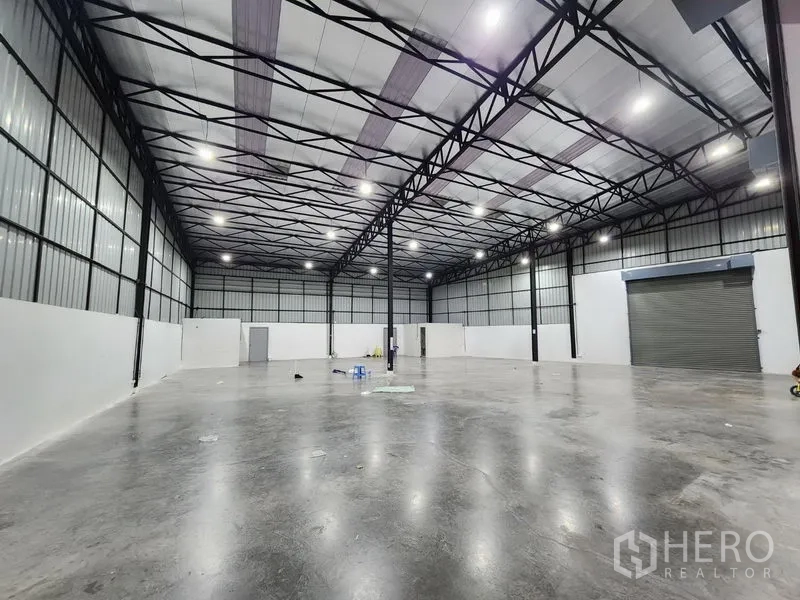Warehouse for rent in Pak Kret, Nonthaburi - Clear‑span storage hall with insulated roof panels, white perimeter walls and a roller shutter entrance.