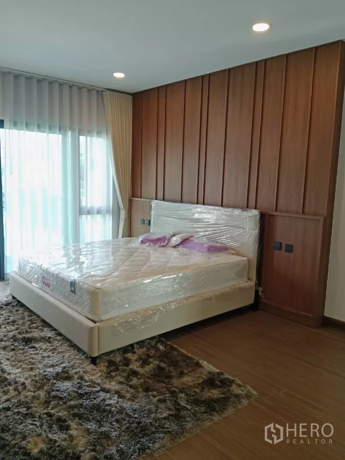 Detached House for rent in Bang Phli, Samut Prakan - Master bedroom with wood accent wall, large bed and plush rug.