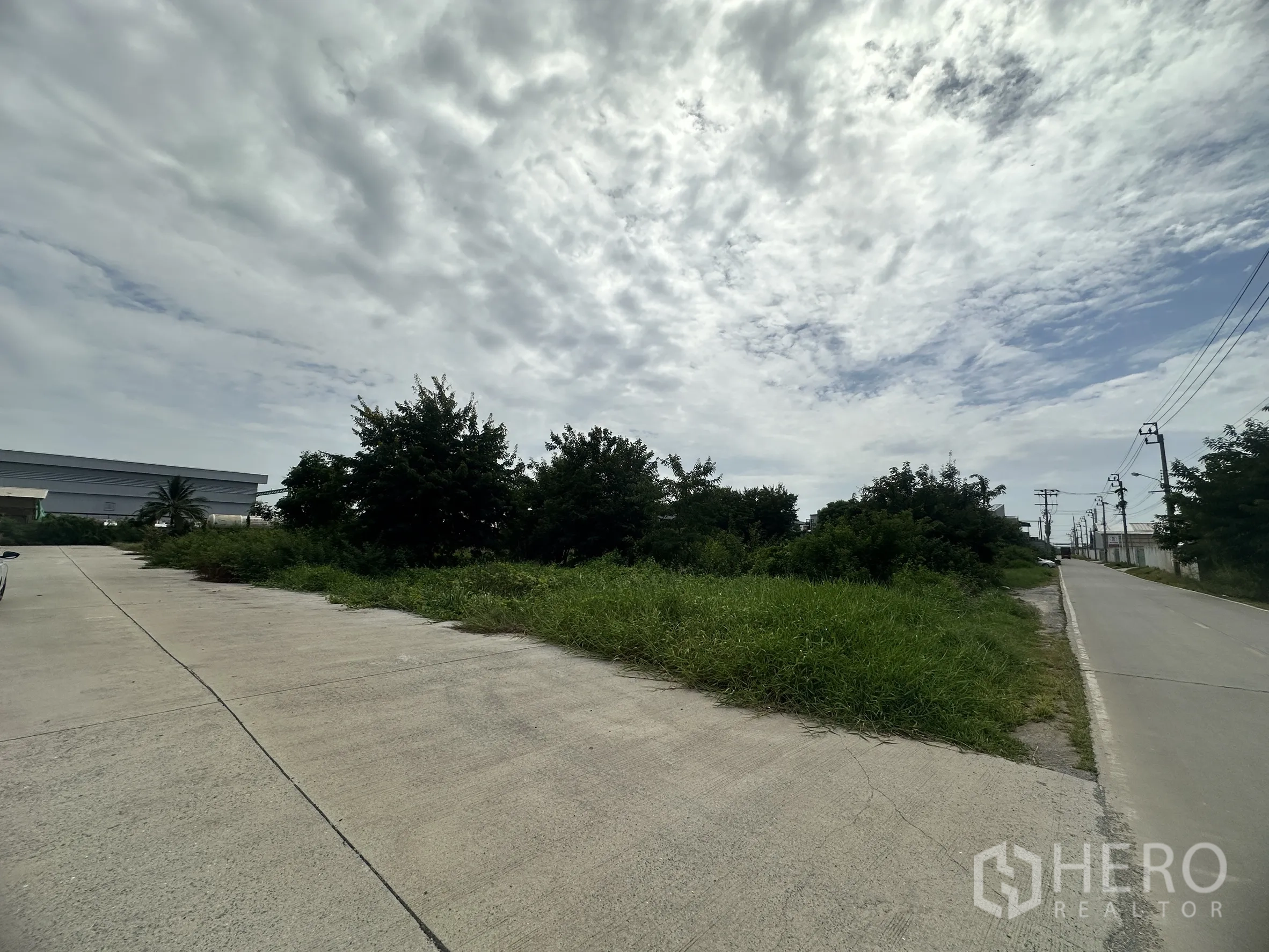 Land for sale in Sai Noi, Nonthaburi - Corner of vacant land next to a public road and concrete driveway with overhead power lines.