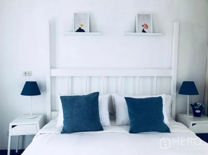 ทาวน์เฮาส์ ให้เช่าในKhlong Toei, Bangkok - ห้องนอนโทนขาวเรียบง่าย เตียงคู่ หมอนสีน้ำเงิน และโคมไฟหัวเตียง