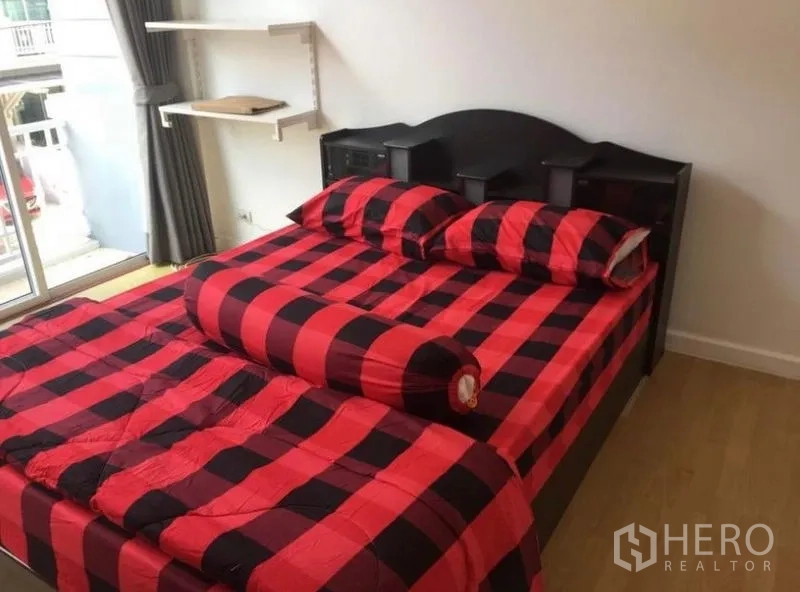 联排别墅 出租在Prawet, Bangkok - 卧室配红黑格子床品，深色床头板，可通往阳台。