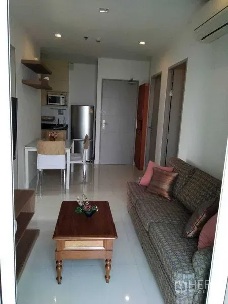 Condominium for rent in Watthana, Bangkok - Open-plan living room with sofa, TV wall unit, dining table, and compact kitchenette.