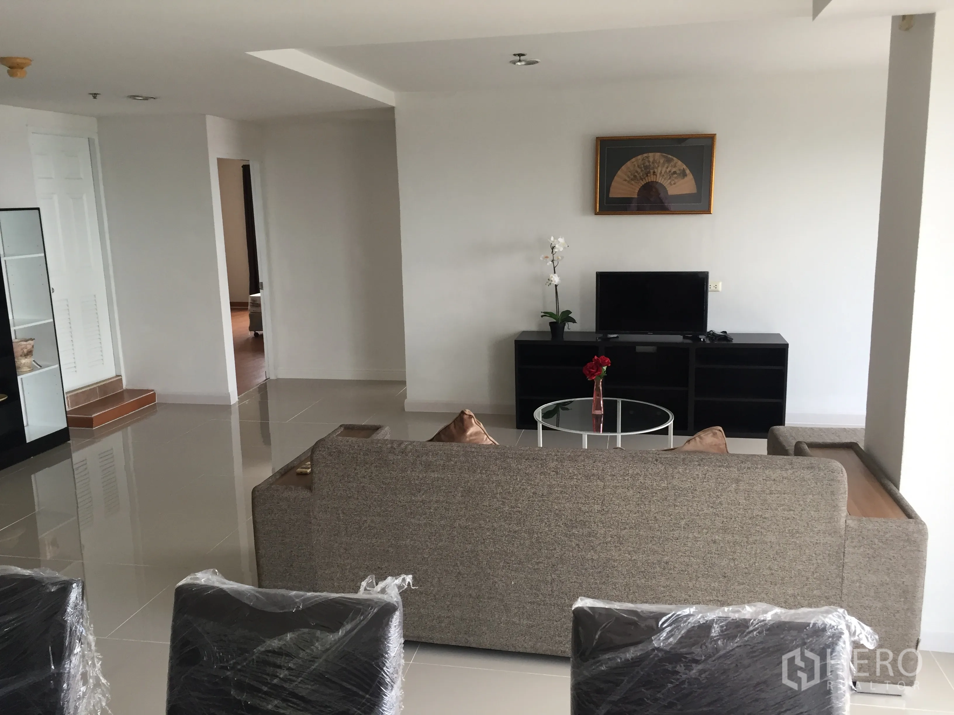 คอนโด ให้เช่าในKhlong Toei, Bangkok - ห้องนั่งเล่นมีโซฟาสีเทา ชั้นวางทีวี โต๊ะกลางกระจก และพื้นกระเบื้องเงา