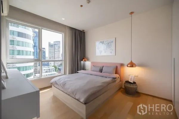Condominium for rent in Watthana, Bangkok - Bedroom with large windows showcasing a city view of nearby high-rise buildings.