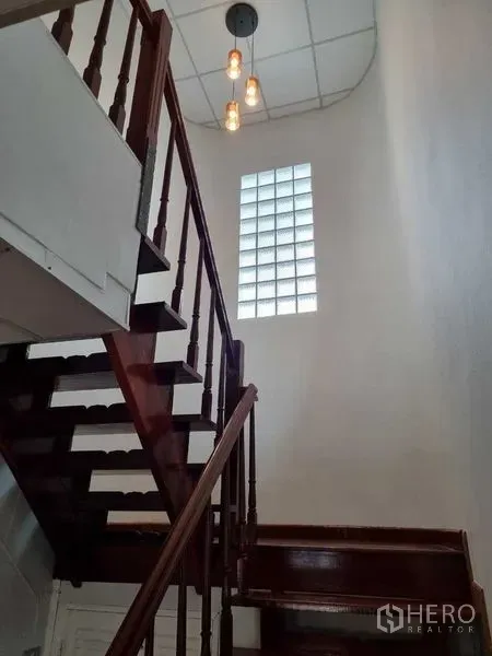 独立式住宅 出租在Mueang Nonthaburi, Nonthaburi - 木质楼梯，吊灯与玻璃砖采光窗。