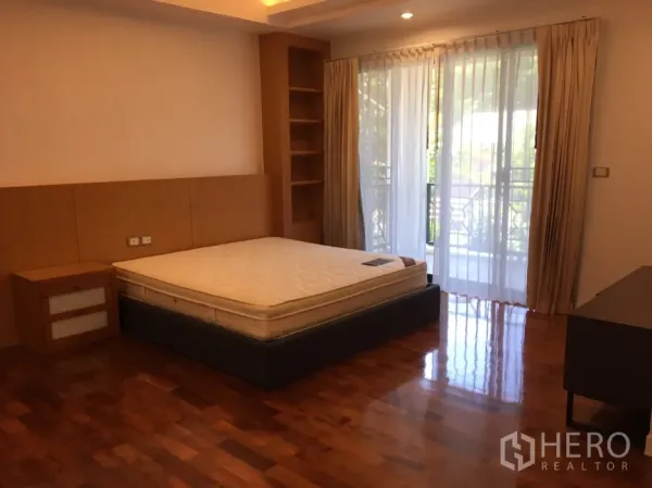 Detached House for rent in Watthana, Bangkok - Bright bedroom with hardwood floors, built-in shelving and sliding glass doors to a balcony with curtains.