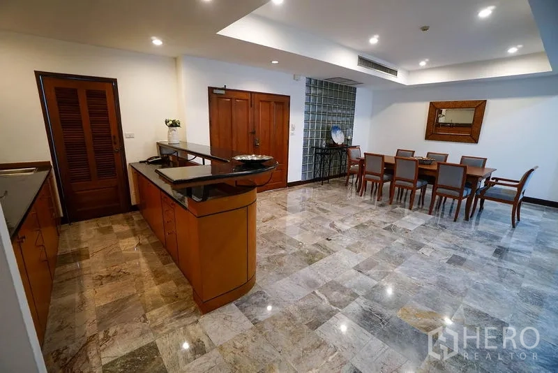 อพาร์ทเมนท์ ให้เช่าในWatthana, Bangkok - ครัวเปิดพร้อมไอส์แลนด์ยาว เคาน์เตอร์หิน และมุมมองไปยังพื้นที่ทานอาหารบนพื้นหินอ่อนขัดมัน.