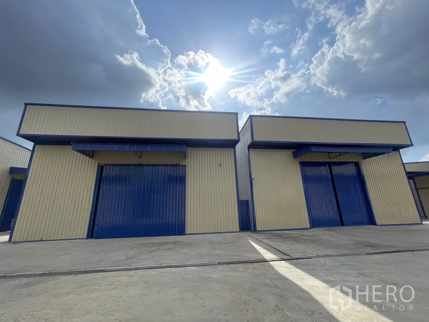 Warehouse for rent in Wang Thonglang, Bangkok - Two warehouse units with large metal sliding doors and a wide concrete yard under a bright sky.