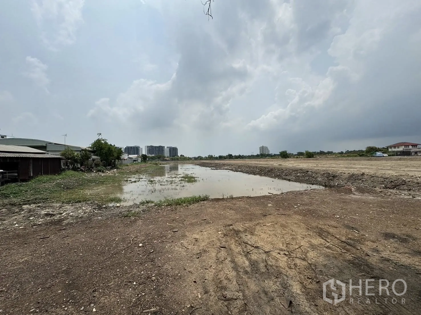 Land for sale in Bang Phli, Samut Prakan - Wide view of a pond beside open land with low-rise homes and condominiums in the distance.
