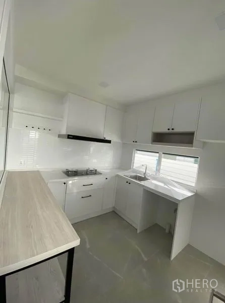 Detached House for rent in Bang Phli, Samut Prakan - Modern white kitchen with L-shaped cabinets, gas hob, range hood and window.