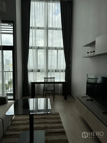 Condominium for rent in Huai Khwang, Bangkok - Bright living room with tall curtains, work desk, TV cabinet and panoramic city outlook.