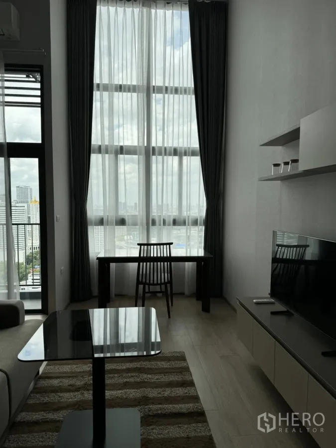 Condominium for rent in Huai Khwang, Bangkok - Bright living room with tall curtains, work desk, TV cabinet and panoramic city outlook.