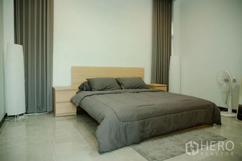 บ้าน ขายในPhra Pradaeng, Samut Prakan - ห้องนอนมาสเตอร์กว้าง ผ้าม่านสีเทา โต๊ะหัวเตียง และพื้นกระเบื้อง