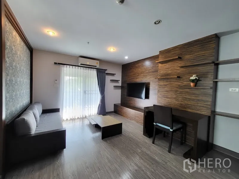 Condominium for rent in Phra Khanong, Bangkok - Cozy living room with TV feature wall, desk, sofa, and balcony with sheer curtains.