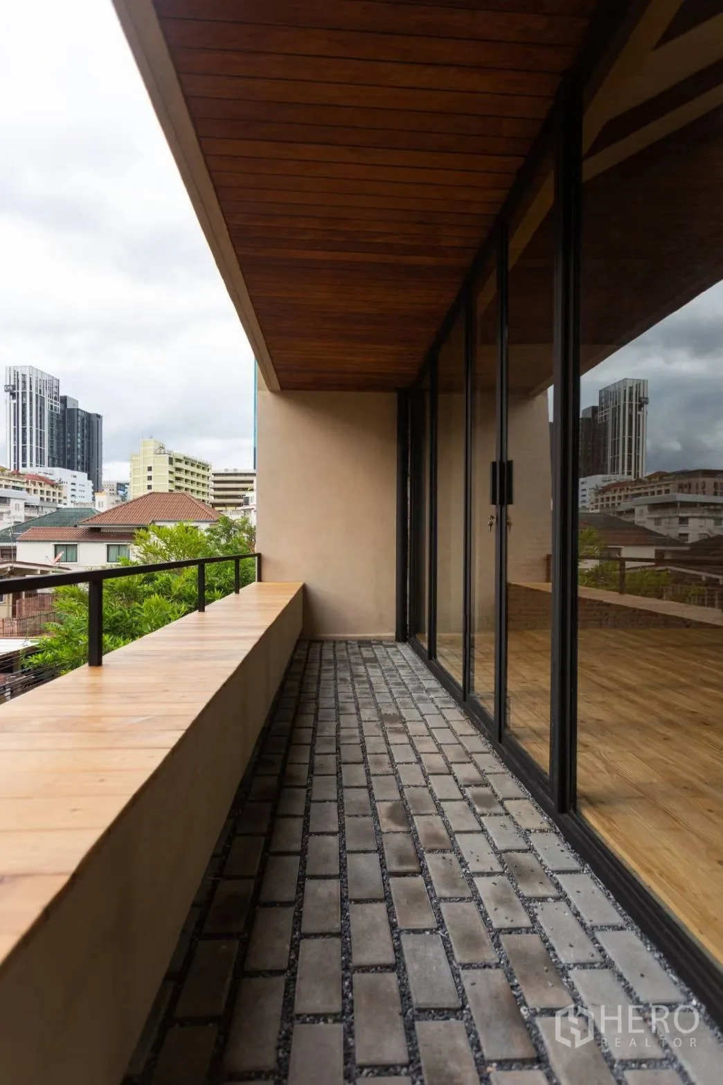 Home Office for rent in Watthana, Bangkok - Shaded balcony with brick pavers and city view beside floor‑to‑ceiling sliding glass doors.