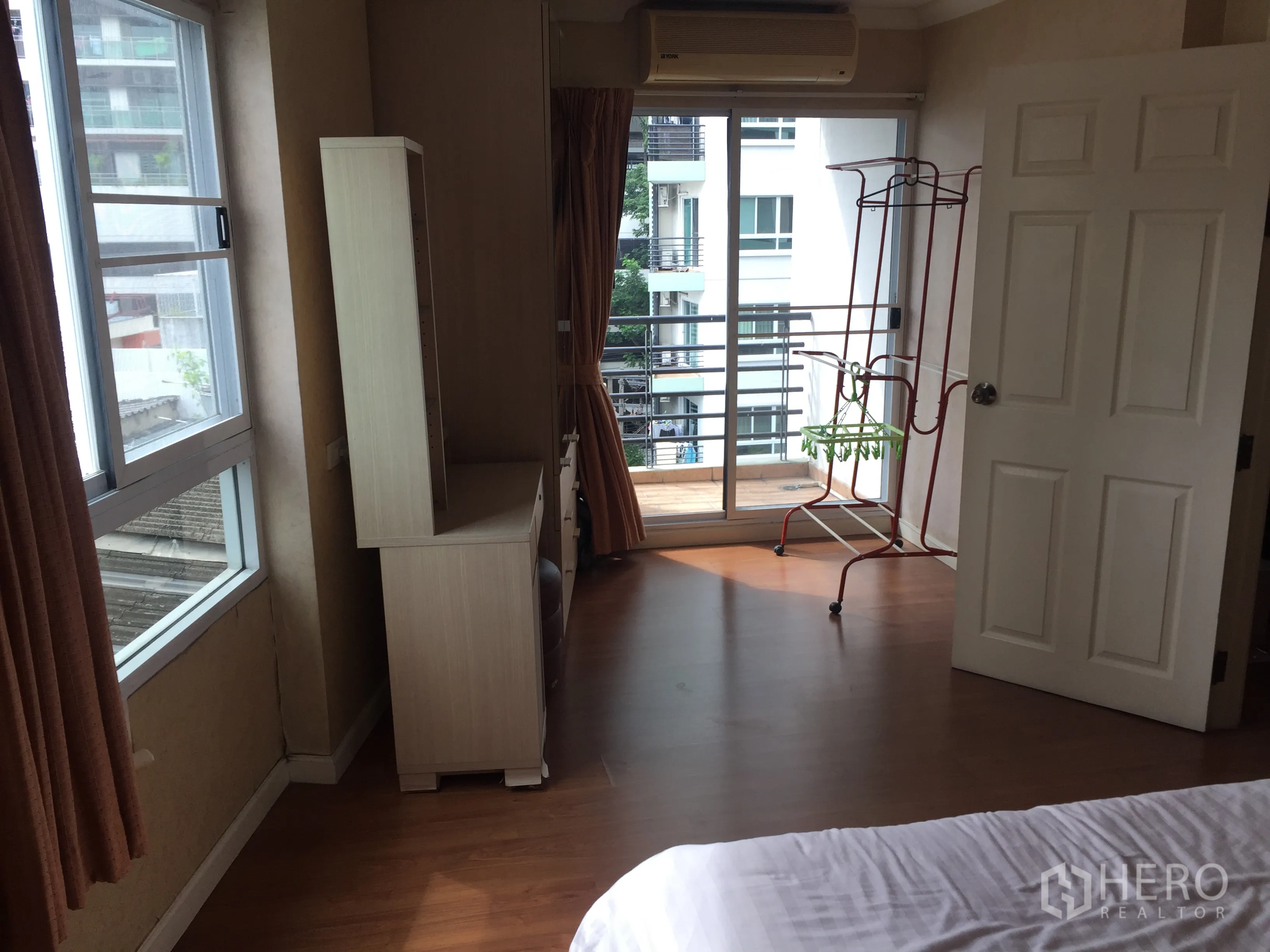 Condominium for rent in Watthana, Bangkok - Bedroom with wood flooring, desk and air conditioner, opening through sliding glass doors to a small balcony.