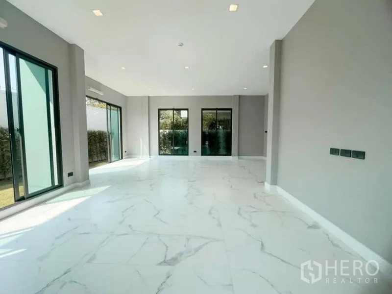Detached House for sale in Mueang Nonthaburi, Nonthaburi - Sunlit living room with large-format white tiles and multiple garden access doors.
