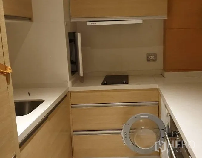 Condominium for sale in Khlong Toei, Bangkok - Compact L-shaped kitchen with light wood cabinets, electric hob, hood, and under-counter appliances.