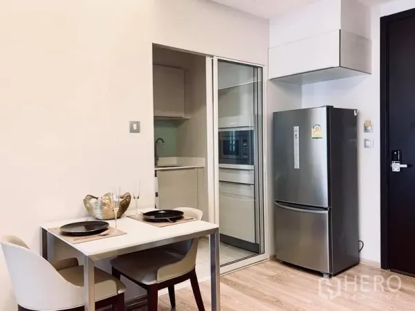 Condominium for rent in Watthana, Bangkok - Two-seat dining area beside a sliding-glass separate kitchen and stainless refrigerator.