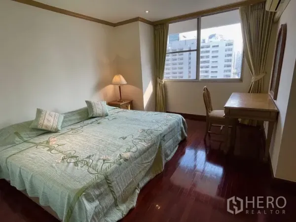 Condominium for rent or sale in Watthana, Bangkok - Guest bedroom with a large bed, writing desk, and city-view window with green curtains.