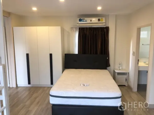 Townhouse for rent or sale in Saphan Sung, Bangkok - Bright bedroom with bed, wardrobe, bedside table and door to an ensuite bathroom.