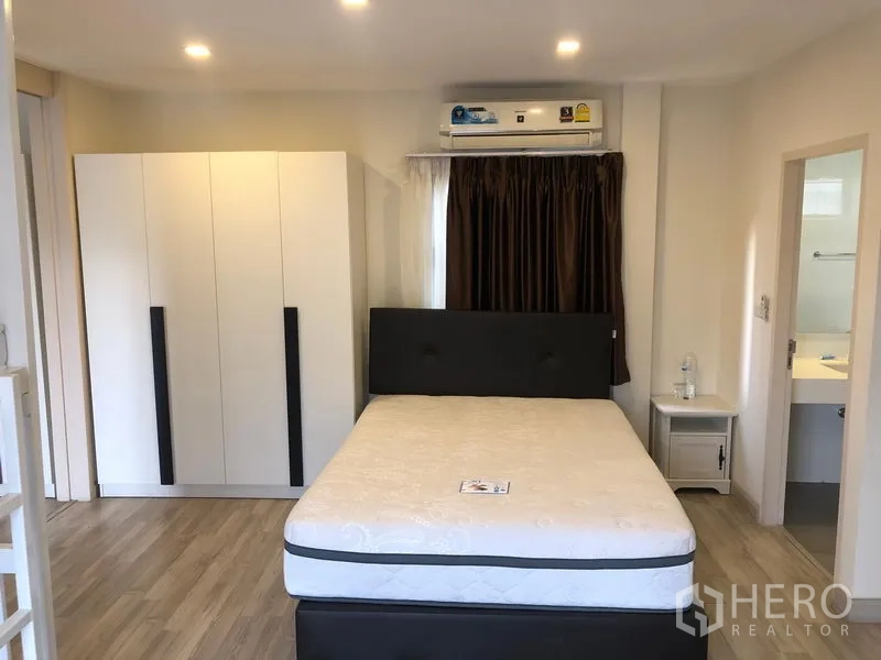 Townhouse for rent or sale in Saphan Sung, Bangkok - Bright bedroom with bed, wardrobe, bedside table and door to an ensuite bathroom.
