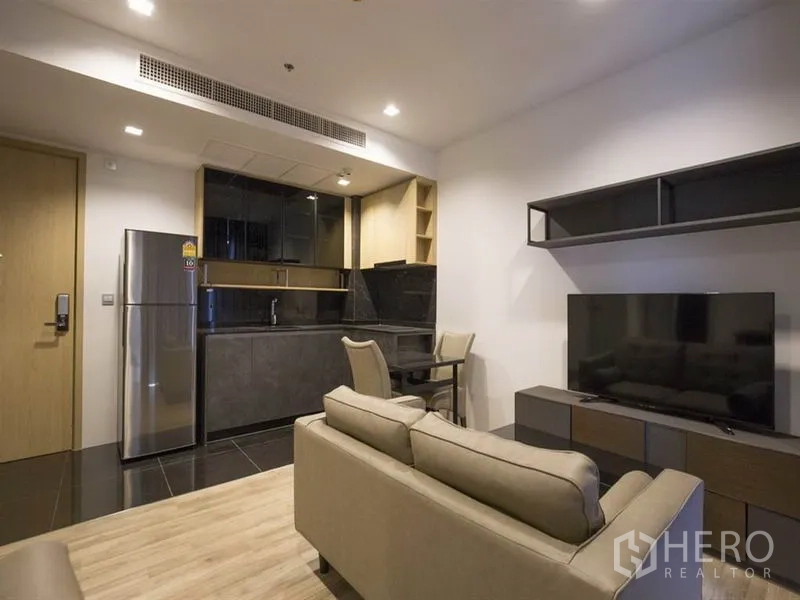 Condominium for rent in Chatuchak, Bangkok - Open-plan living area with sofa, TV console, and built-in kitchen with fridge and dining nook.