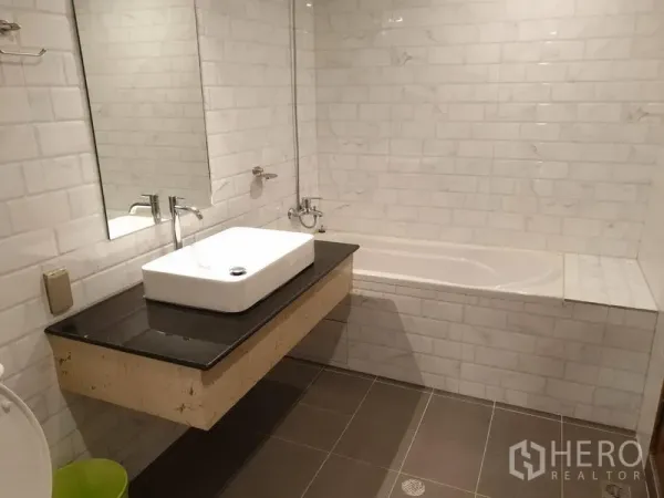 คอนโด ให้เช่าในWatthana, Bangkok - ห้องน้ำสมัยใหม่ ผนังกระเบื้องลายอิฐสีขาว อ่างอาบน้ำ อ่างล้างหน้าวางบนท็อปหินสีดำ และกระจกบานใหญ่