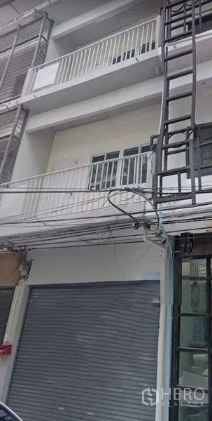 อาคารพาณิชย์ ให้เช่าในKhlong Toei, Bangkok - ด้านหน้าอาคารพาณิชย์ 4 ชั้น หน้าร้านประตูม้วน ระเบียงราวเหล็ก โทนสีเทาขาว พร้อมสายไฟริมถนน