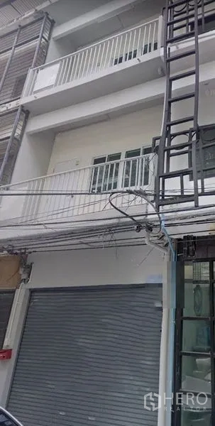 อาคารพาณิชย์ ให้เช่าในKhlong Toei, Bangkok - ด้านหน้าอาคารพาณิชย์ 4 ชั้น หน้าร้านประตูม้วน ระเบียงราวเหล็ก โทนสีเทาขาว พร้อมสายไฟริมถนน