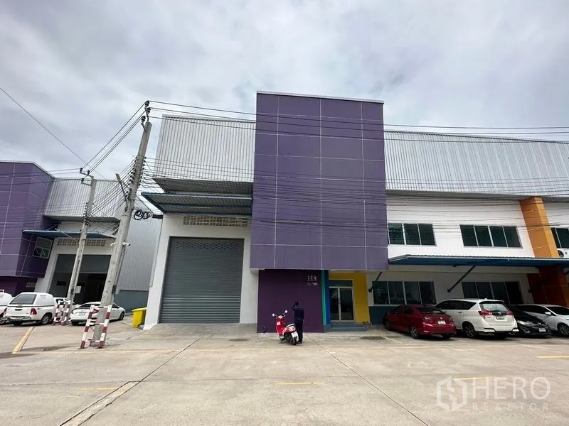 โรงงาน ให้เช่าในBang Phli, Samut Prakan - ด้านหน้าอาคารพร้อมครีบสีม่วง ประตูม้วน และที่จอดรถมีหลังคา