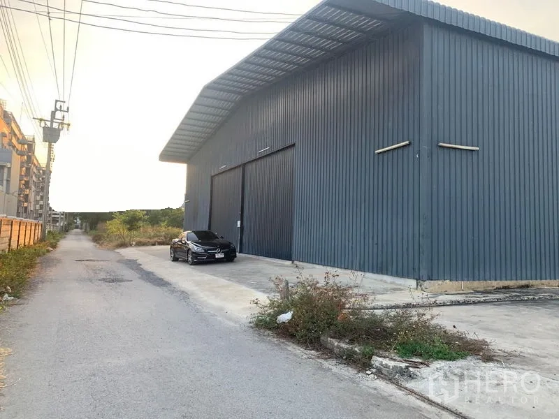 货栈 出租在Khan Na Yao, Bangkok - 沿安静小路的金属板仓库侧立面，带停车区域和电线杆。