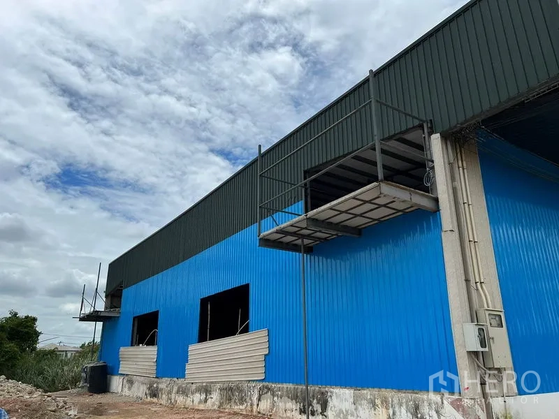 Warehouse for rent in Lat Krabang, Bangkok - Side view of blue warehouse with elevated loading platform and partially installed wall panels.
