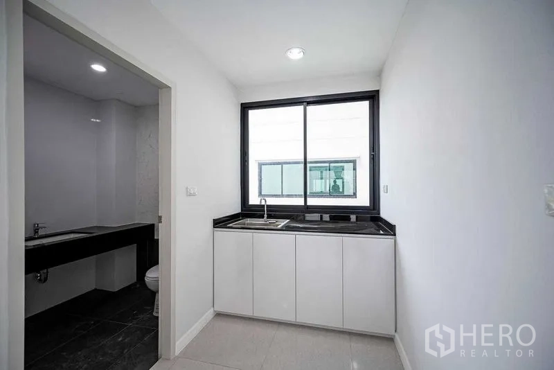 Home Office for rent in Suan Luang, Bangkok - Small pantry with window and black countertop adjacent to a tiled washroom.